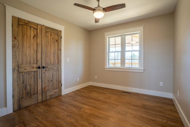 empty room with a ceiling fan, baseboards, visible vents, and wood finished floors