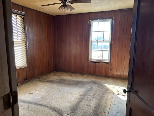 empty room featuring carpet flooring, ceiling fan, and wooden walls