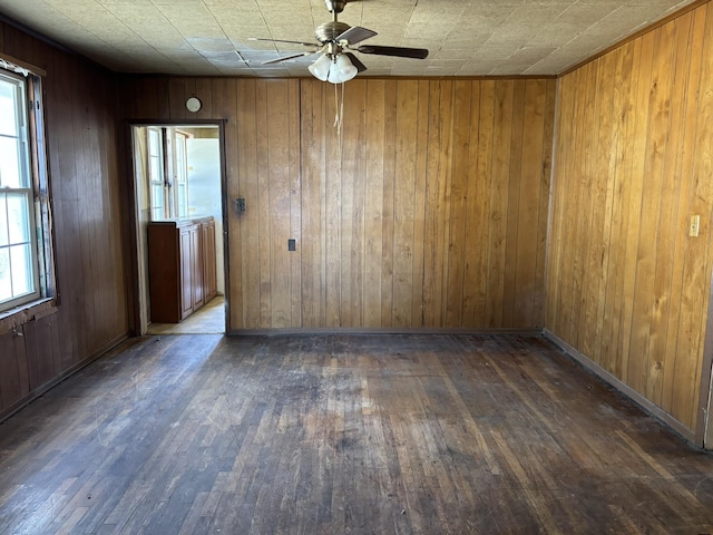 spare room with hardwood / wood-style flooring, ceiling fan, wooden walls, and baseboards