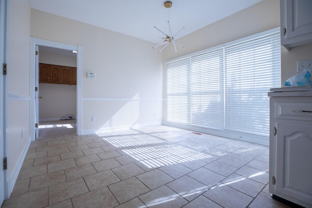 unfurnished dining area featuring baseboards, tile patterned floors, and an inviting chandelier