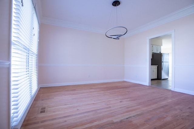 spare room featuring light wood-style floors, visible vents, crown molding, and baseboards