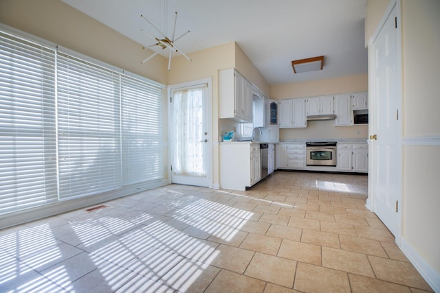 kitchen featuring light tile patterned flooring, under cabinet range hood, stainless steel appliances, white cabinetry, and light countertops