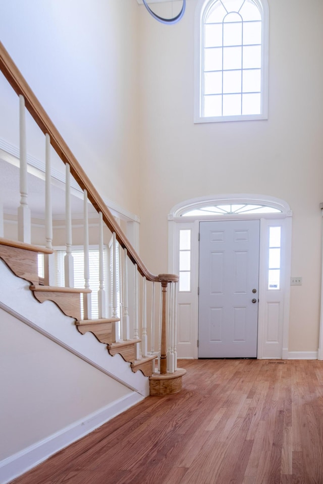 entrance foyer featuring stairs, light wood finished floors, a towering ceiling, and baseboards