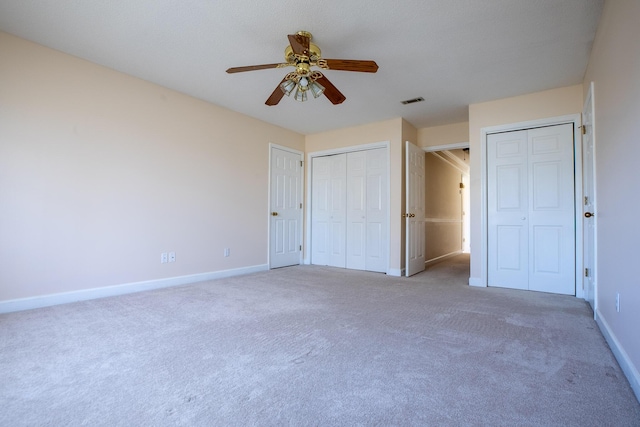 unfurnished bedroom with carpet, visible vents, baseboards, and two closets