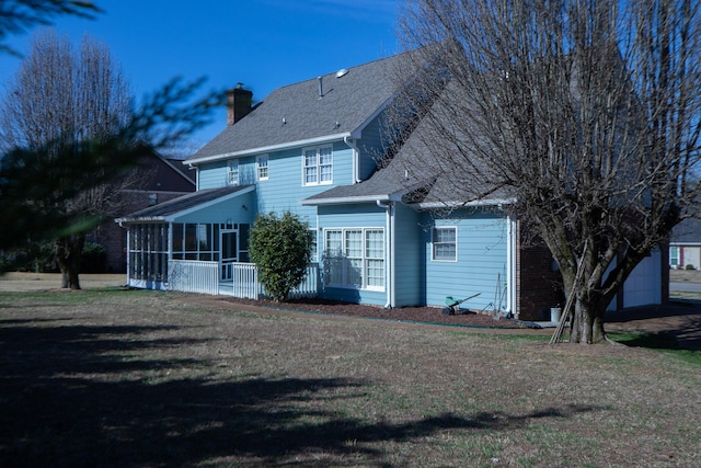 back of property with a garage, a lawn, a chimney, and a sunroom