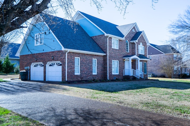 traditional-style house with aphalt driveway, brick siding, roof with shingles, a front yard, and a garage