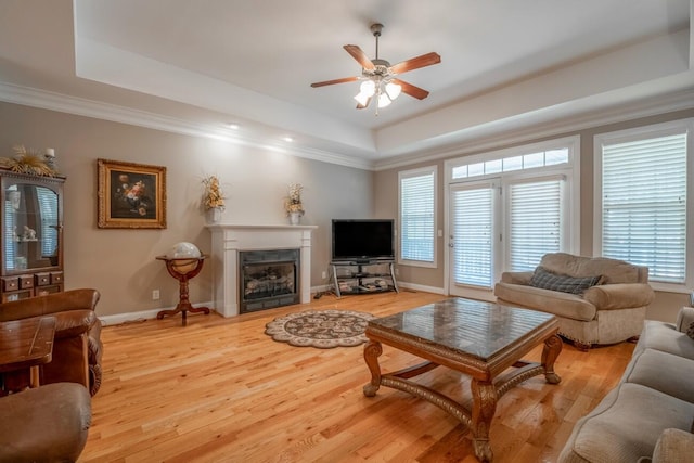 living area with a raised ceiling, light wood-style floors, a high end fireplace, ornamental molding, and baseboards