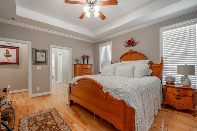 bedroom featuring a raised ceiling, multiple windows, and light wood-style flooring