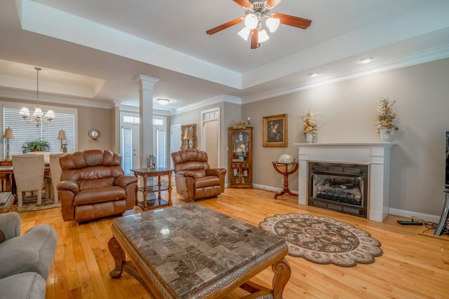 living room featuring a tray ceiling, baseboards, a fireplace, and light wood finished floors