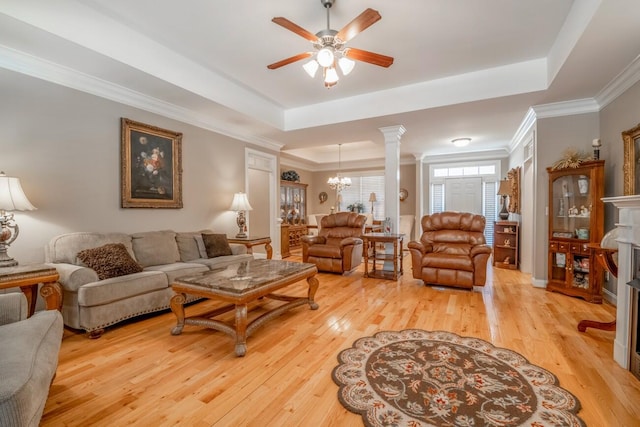 living room with a tray ceiling, light wood-type flooring, a fireplace, and crown molding