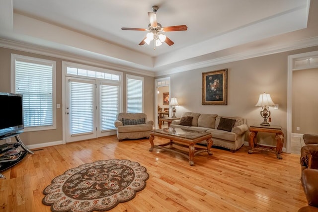 living area featuring ornamental molding, a tray ceiling, and light wood-style floors