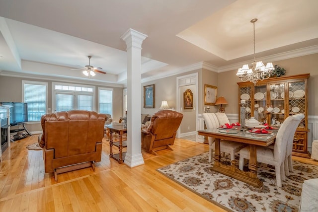 dining room with a raised ceiling, light wood finished floors, ornate columns, and ceiling fan with notable chandelier