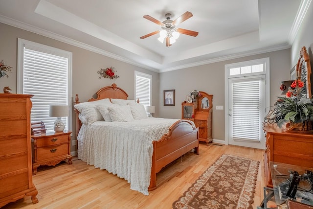 bedroom featuring light wood-style floors, ornamental molding, a raised ceiling, and a ceiling fan