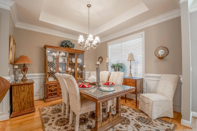 dining room with a tray ceiling, a wainscoted wall, light wood finished floors, a decorative wall, and an inviting chandelier