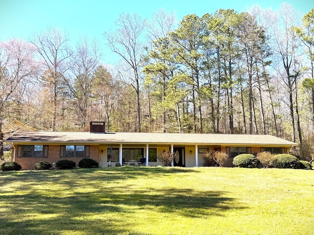 single story home with brick siding, a chimney, and a front yard