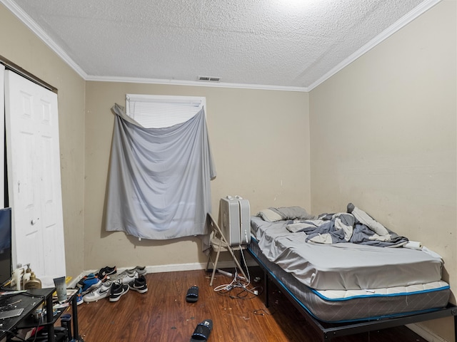 bedroom with a textured ceiling, ornamental molding, wood finished floors, and visible vents