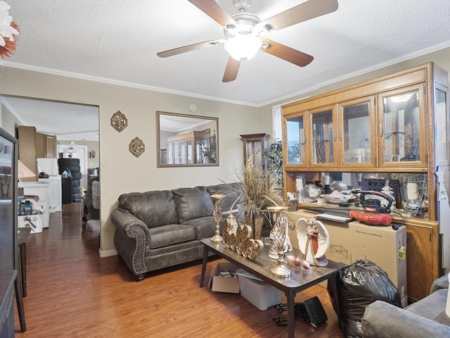 living room featuring a ceiling fan, a textured ceiling, ornamental molding, and wood finished floors