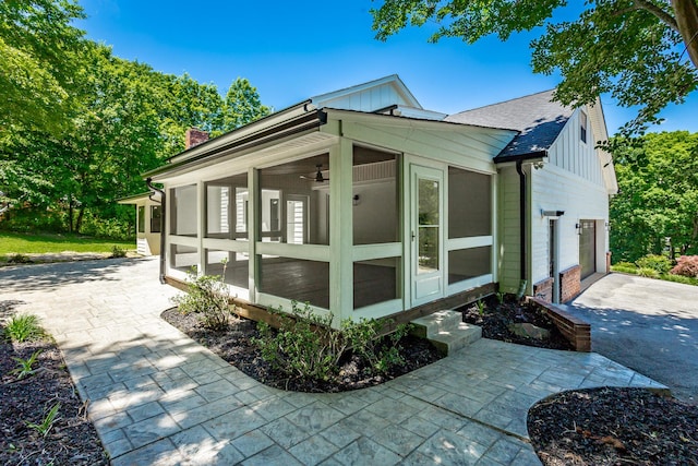 view of home's exterior featuring roof with shingles, board and batten siding, a sunroom, a garage, and driveway