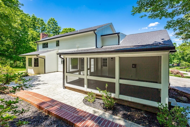 rear view of property with a patio area, a chimney, a sunroom, and roof with shingles