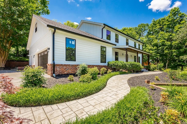 view of front of house featuring an attached garage, covered porch, concrete driveway, and brick siding