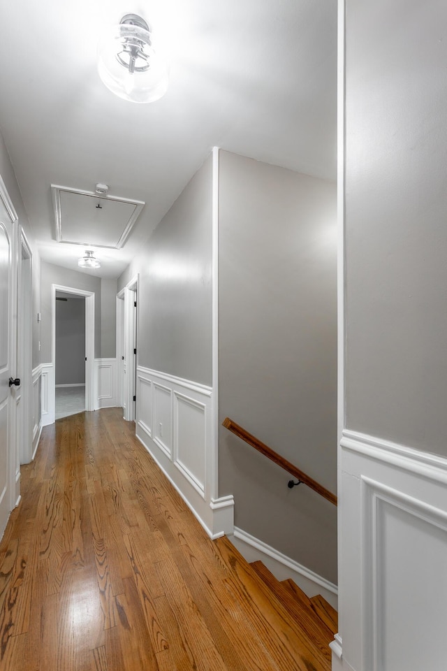 corridor featuring a decorative wall, attic access, wainscoting, an upstairs landing, and wood finished floors