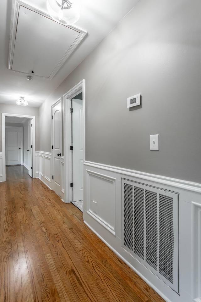 hall featuring attic access, visible vents, wainscoting, wood finished floors, and a decorative wall