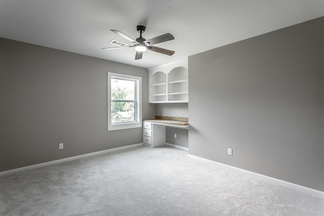 spare room with light carpet, visible vents, a ceiling fan, baseboards, and built in desk