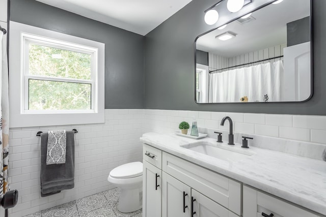 full bathroom with tile walls, visible vents, toilet, wainscoting, and vanity