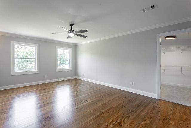 spare room featuring dark wood finished floors, crown molding, visible vents, a ceiling fan, and baseboards