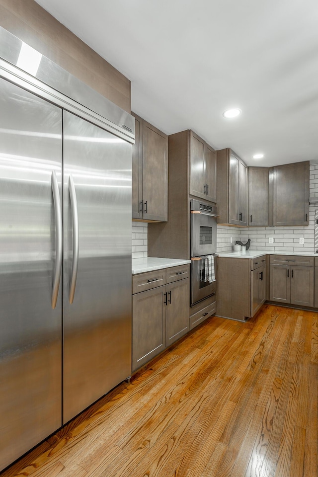 kitchen with stainless steel appliances, light wood-type flooring, light countertops, and tasteful backsplash