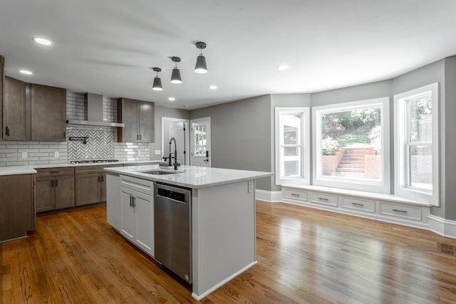 kitchen with a sink, wall chimney range hood, appliances with stainless steel finishes, decorative backsplash, and dark wood finished floors