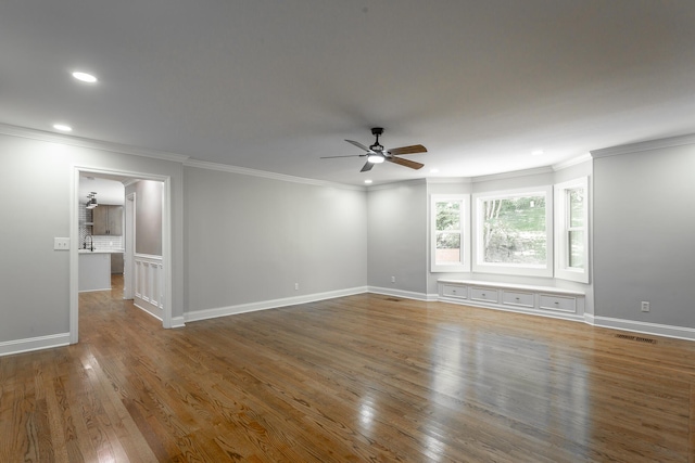 empty room featuring crown molding, visible vents, a ceiling fan, wood finished floors, and baseboards