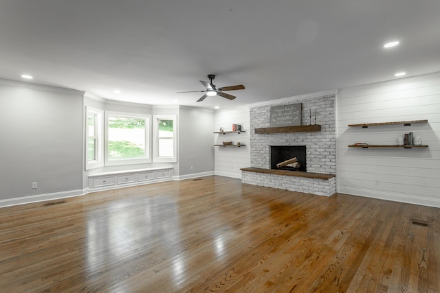 unfurnished living room featuring a brick fireplace, crown molding, visible vents, and wood finished floors