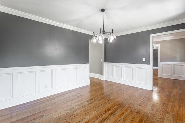 empty room featuring ornamental molding, wainscoting, an inviting chandelier, and wood finished floors