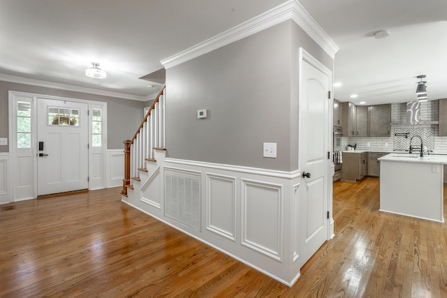 entryway with visible vents, ornamental molding, stairway, wainscoting, and light wood finished floors