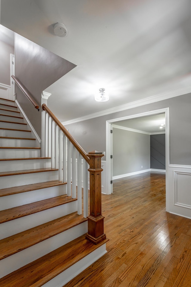 stairs featuring ornamental molding, a wainscoted wall, and wood finished floors