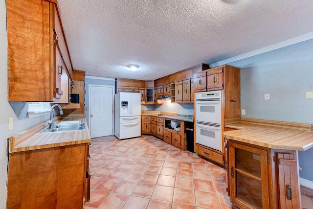 kitchen featuring white appliances, brown cabinetry, ornamental molding, a peninsula, and a sink