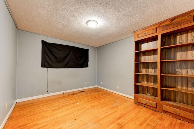 empty room with a textured ceiling, light wood finished floors, and baseboards