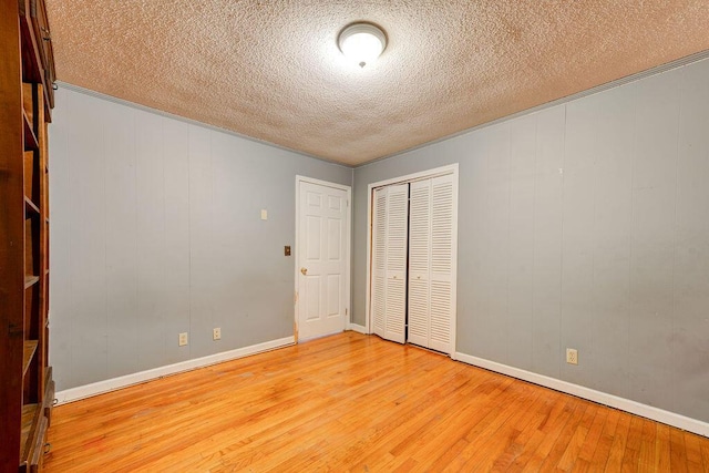 unfurnished bedroom with light wood-type flooring, a textured ceiling, baseboards, and a closet