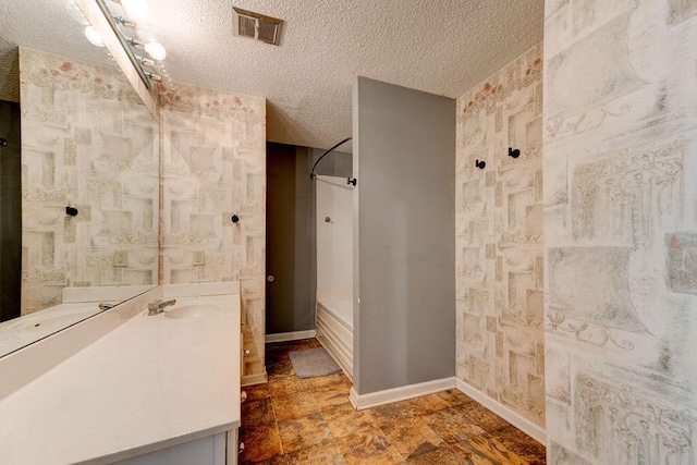 full bath featuring a textured ceiling, vanity, visible vents, baseboards, and stone finish floor