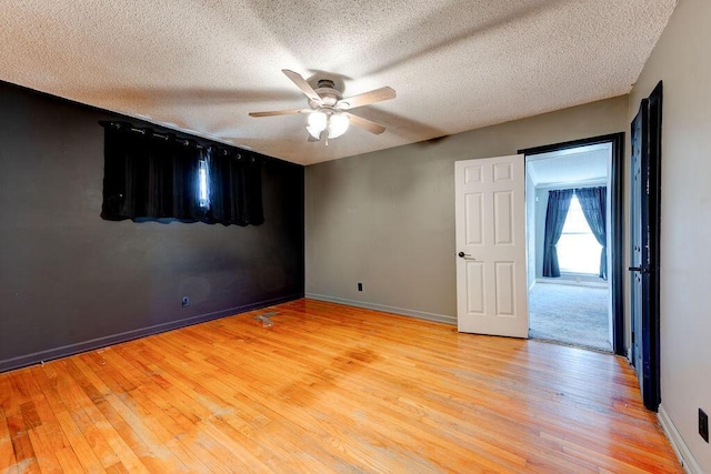 unfurnished room featuring baseboards, ceiling fan, a textured ceiling, and light wood finished floors