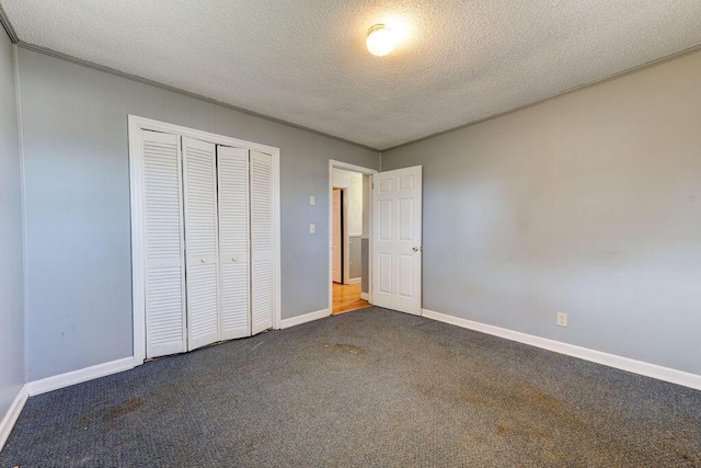 unfurnished bedroom featuring a textured ceiling, baseboards, dark colored carpet, and a closet