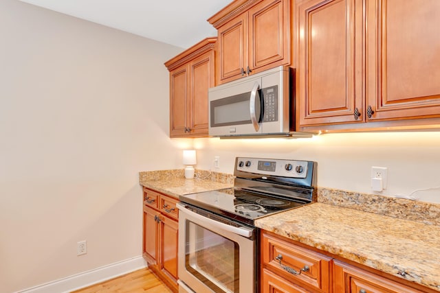 kitchen featuring stainless steel appliances, brown cabinets, light stone counters, and baseboards