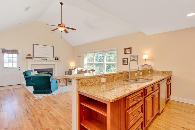 kitchen featuring light wood-style flooring, a sink, stainless steel dishwasher, open shelves, and a glass covered fireplace