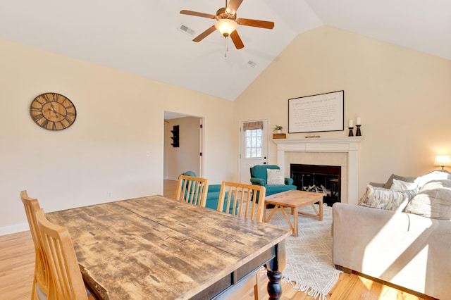 dining area featuring high vaulted ceiling, light wood-type flooring, a fireplace, and visible vents