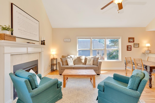 living area featuring baseboards, a ceiling fan, a tile fireplace, lofted ceiling, and wood finished floors