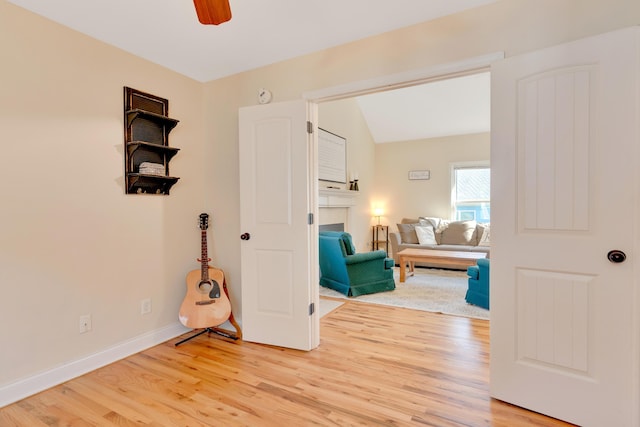 living area with a fireplace, a ceiling fan, baseboards, vaulted ceiling, and light wood-style floors