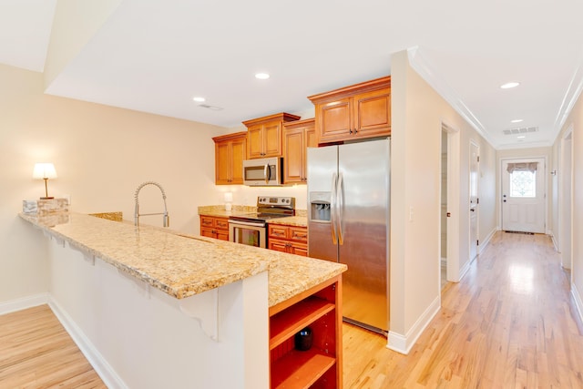 kitchen featuring light wood finished floors, baseboards, appliances with stainless steel finishes, a breakfast bar area, and a peninsula