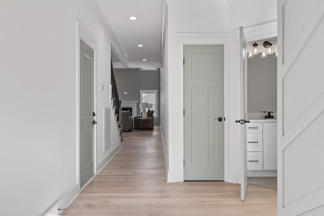 corridor featuring light wood-style flooring, baseboards, crown molding, and recessed lighting