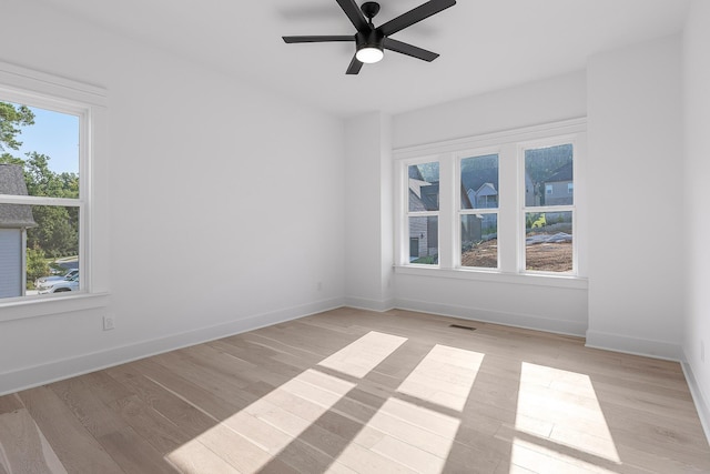 empty room with a ceiling fan, visible vents, light wood-style flooring, and baseboards